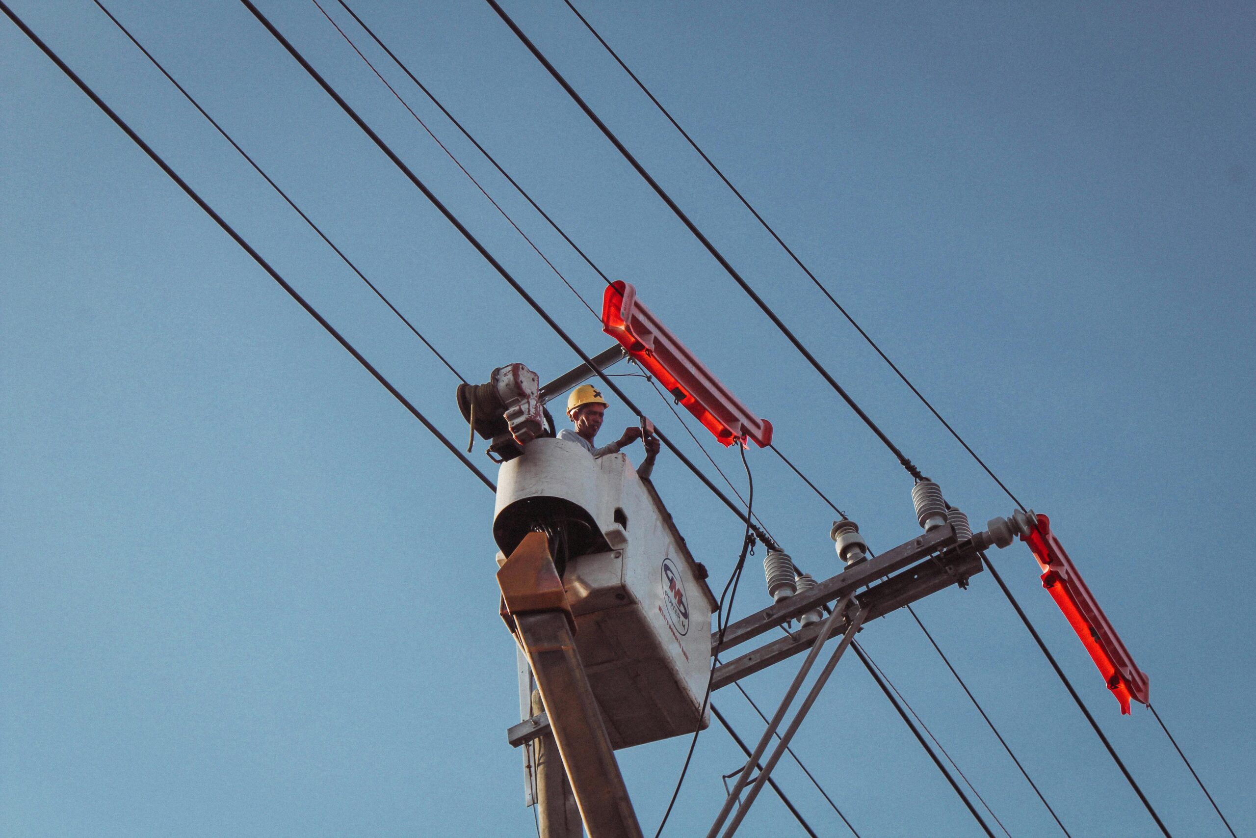 Electrician in a lift repairing overhead power lines on a clear day.